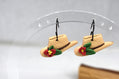 A pair of small cowboy hat earrings with red flowers and green leaves, hanging from black hooks on a clear acrylic display stand.
