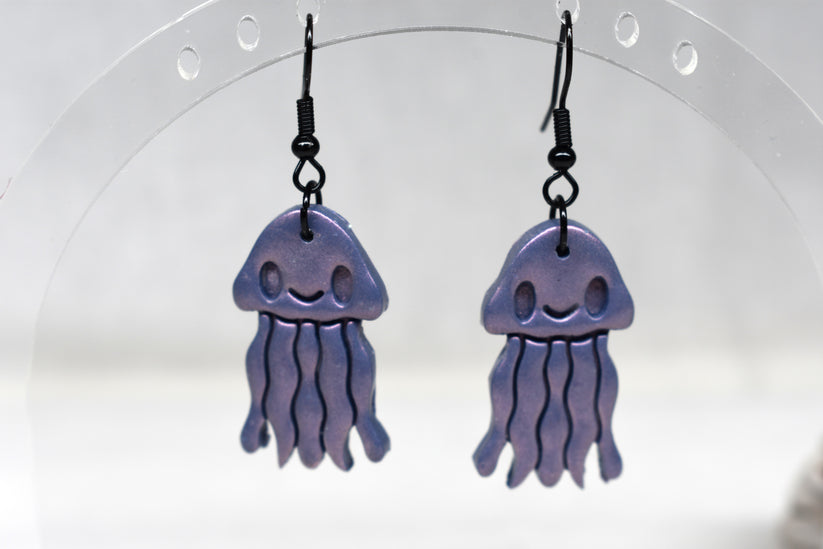 Handmade pearlescent lavender polymer clay smiley jellyfish earrings with flowing tentacles on matte black hooks